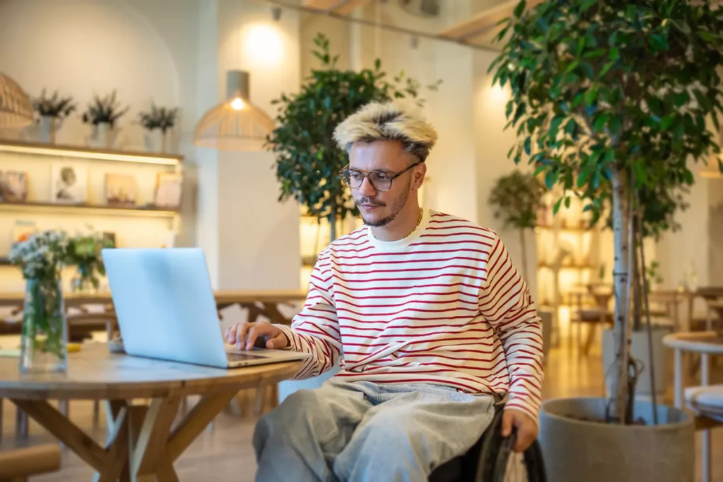 A disabled man sitting in his wheelchair looking at his laptop inside a café